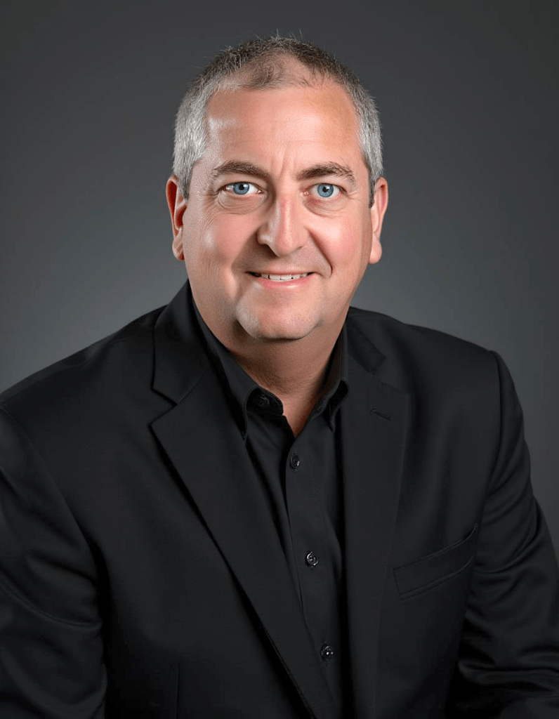 Portrait of a man with short gray hair and blue eyes, wearing a black suit jacket. The neutral background emphasizes a professional appearance.