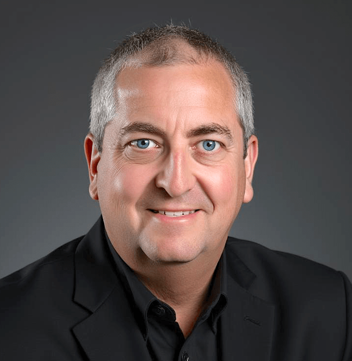 Portrait of a man with short gray hair and blue eyes, wearing a black suit. He smiles against a neutral gray background, conveying professionalism.