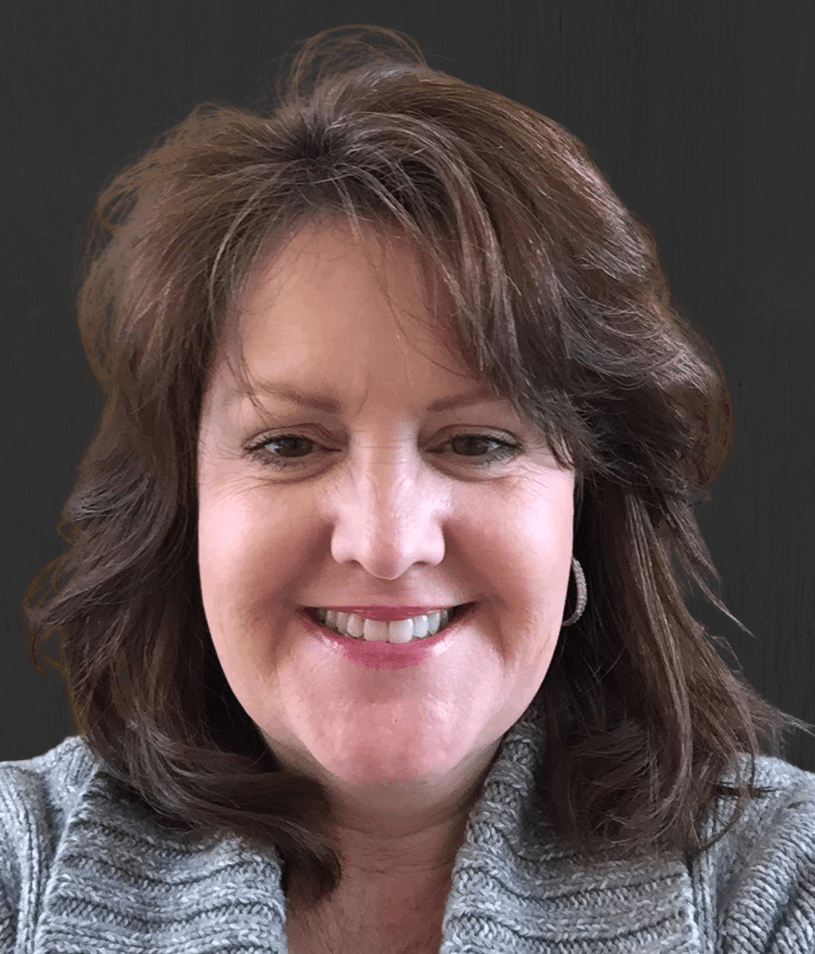 Smiling woman with brown, wavy hair in a gray sweater against a dark background. Reflects warmth and approachability, suitable for a professional context.