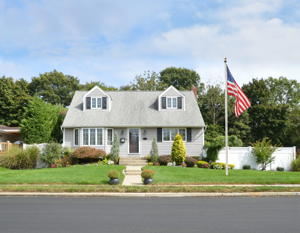 Charming suburban home with gray siding, white trim, and a well-kept garden. An American flag stands proudly in the front yard, enhancing the welcoming vibe.